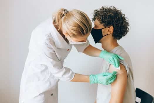 measles, A healthcare worker gives a vaccine shot to a patient wearing a mask, highlighting medical safety and health precautions.