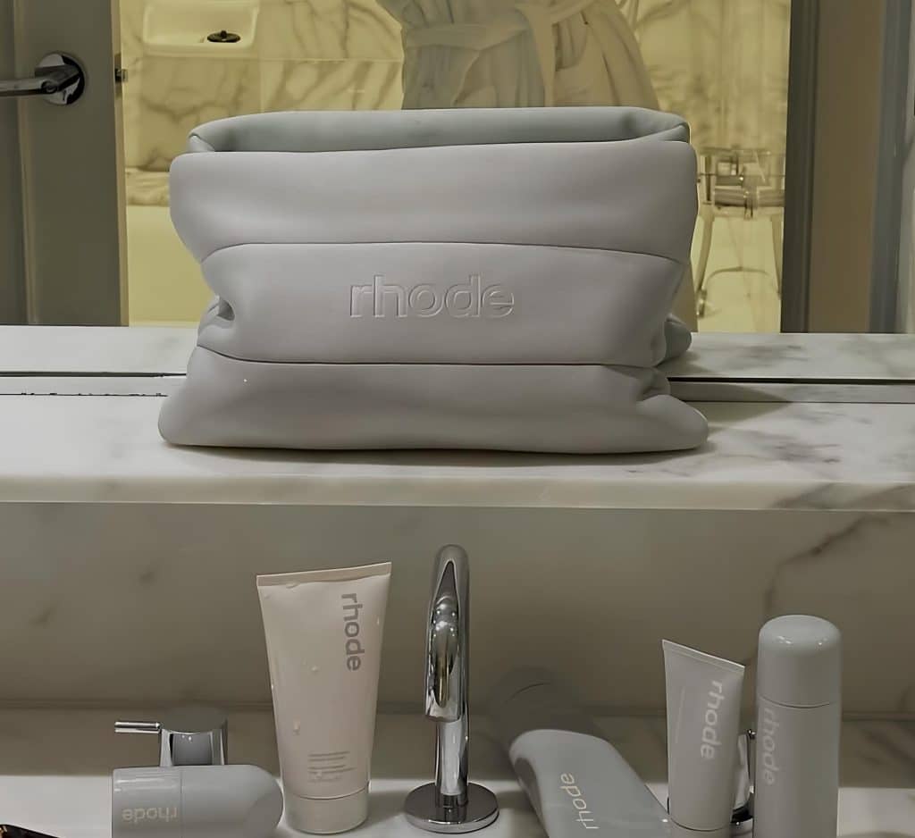Hailey Bieber's Rhode beauty products laid out on a sink with gray makeup bag