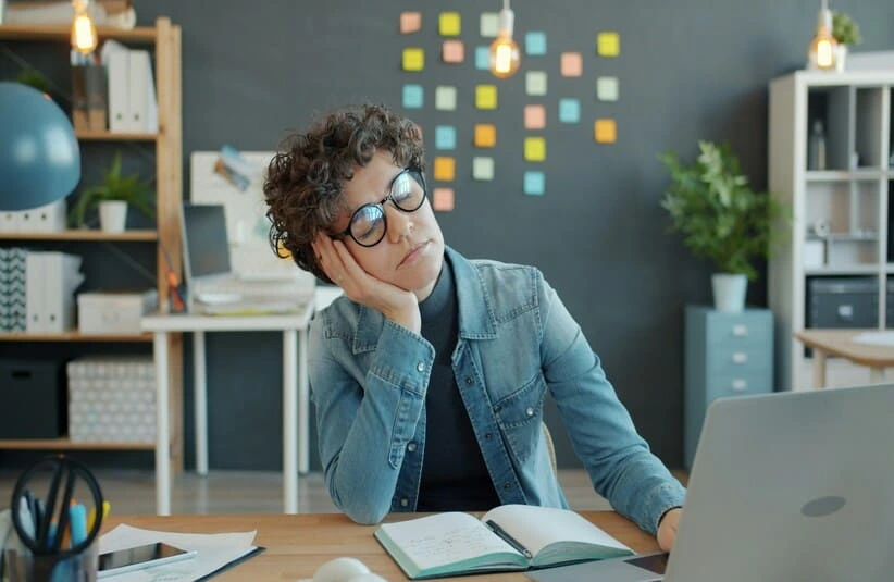 A worker experiencing burnout at their work desk. a woman reading a book in front of a computer.