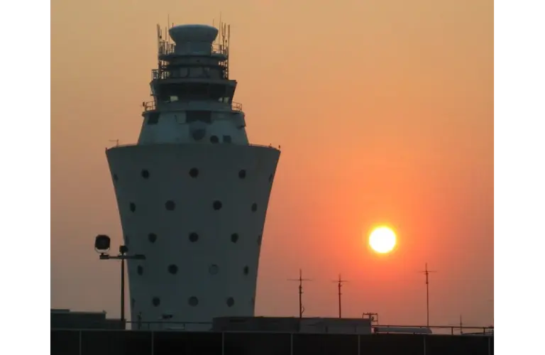 Sunset behind an airport control tower at Laguardia, casting a warm orange glow in the sky. The tower's silhouette adds contrast and a calm ambiance. The airport is shut down due to a collision with an Air Canada flight.