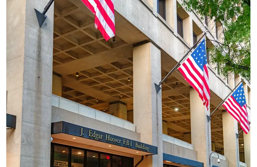 FBI Building in Washington D.C. with the title J. Edgar Hoover F.B.I. Building written above the door with two American flags waving above.