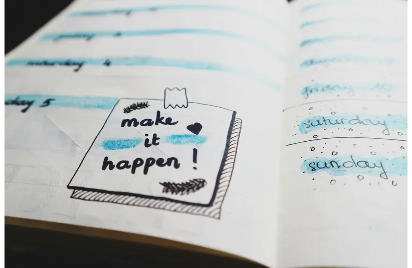 Open planner with a motivational note reading "make it happen!" decorated with doodles. Days of the week highlighted in blue, conveying positivity.
