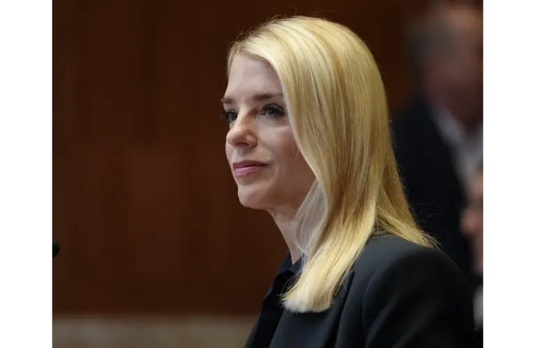 Former Attorney General, Pamela Bondi, with long blonde hair and a focused expression is seated indoors, wearing a dark blazer. The background is softly blurred, creating a professional tone.