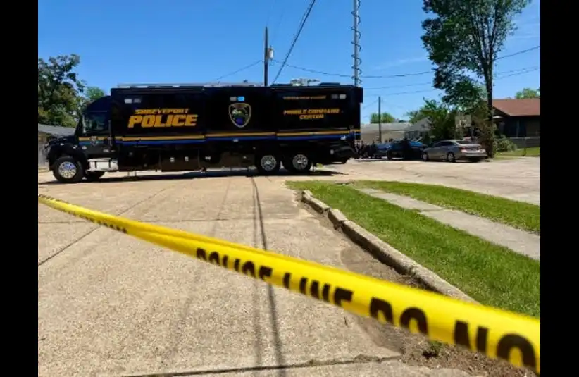 Police command vehicle parked on a suburban street is cordoned off by yellow police tape. The scene conveys a serious and restricted access tone in Shreveport, La.