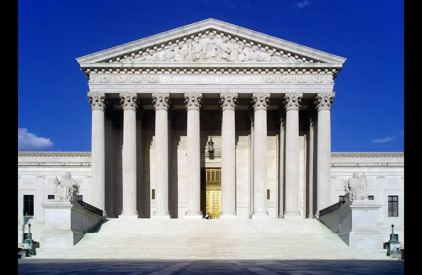 The image shows the U.S. Supreme Court building, featuring its grand façade with tall Corinthian columns, a wide staircase, and intricate sculptures.