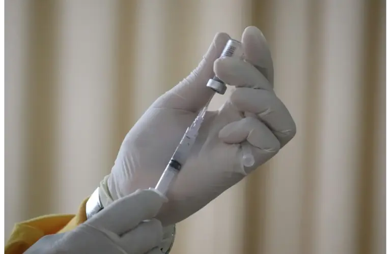 A gloved hand holds a syringe filled with clear liquid against a blurred, neutral background. The tone is clinical and focused. Human clinical trials for opioids are starting soon.