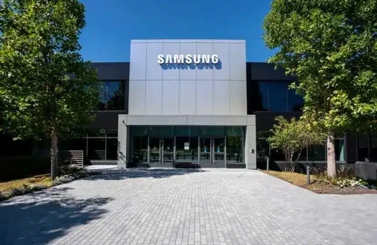 Modern Samsung building exterior with a reflective facade, surrounded by trees under a clear blue sky, conveying a sense of innovation and professionalism.