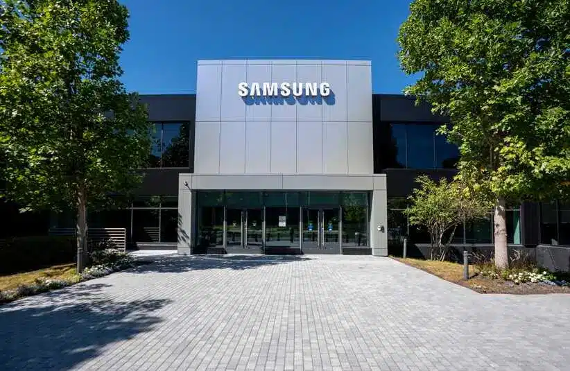 Modern Samsung building exterior with a reflective facade, surrounded by trees under a clear blue sky, conveying a sense of innovation and professionalism.