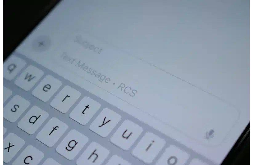 Close-up of a smartphone screen displaying a messaging app interface. The keyboard is visible, with "Text Message · RCS" in the input field.