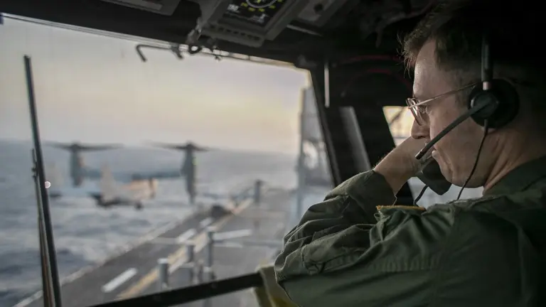 Naval officer aboard USS Tripoli (LHA 7) oversees flight operations from the control tower as the amphibious assault ship sails in the Arabian Sea during blockade in the Strait of Hormuz