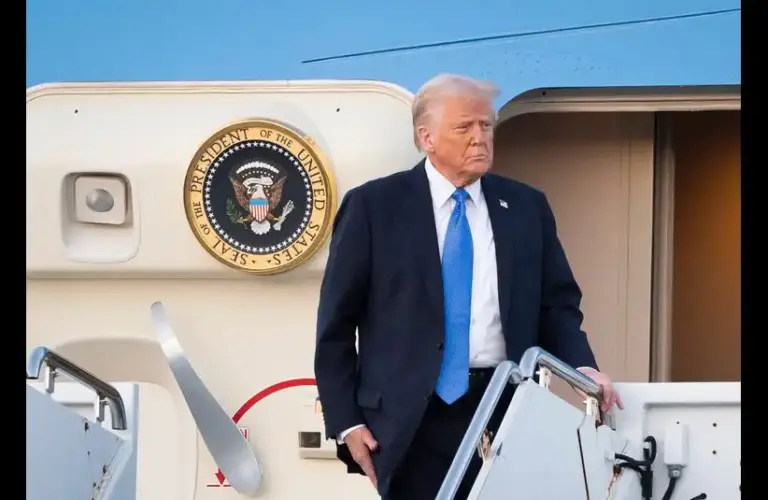 President Donald Trump descends the steps of an aircraft with the Presidential Seal visible. The expression is serious and focused.
