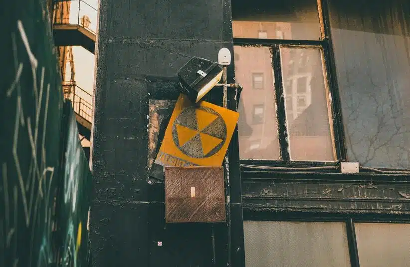 To symbolize the radioactive properties of Uranium, vintage radioactive warning sign on an urban building wall, exuding a rustic industrial vibe.