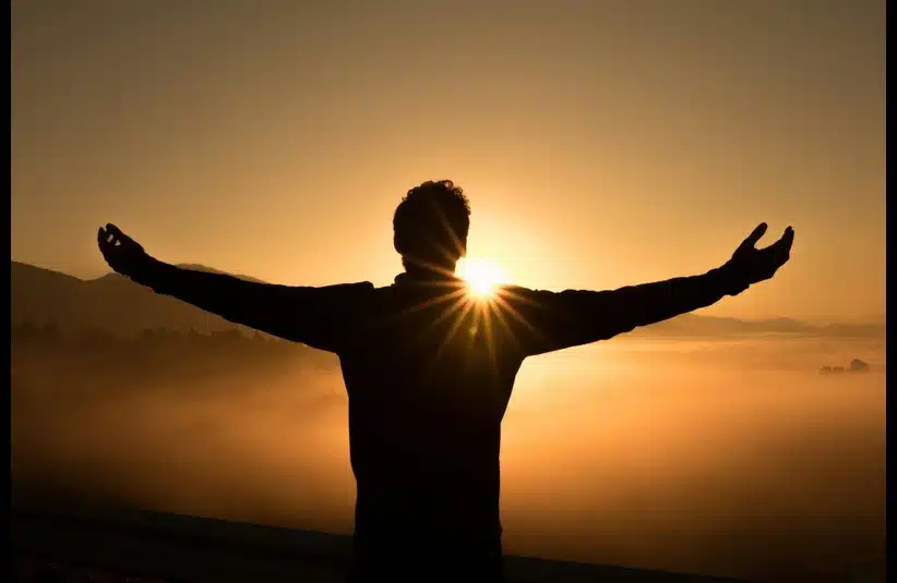 Silhouette of a person with outstretched arms, embracing a sunrise over foggy hills, conveying a sense of freedom and serenity.