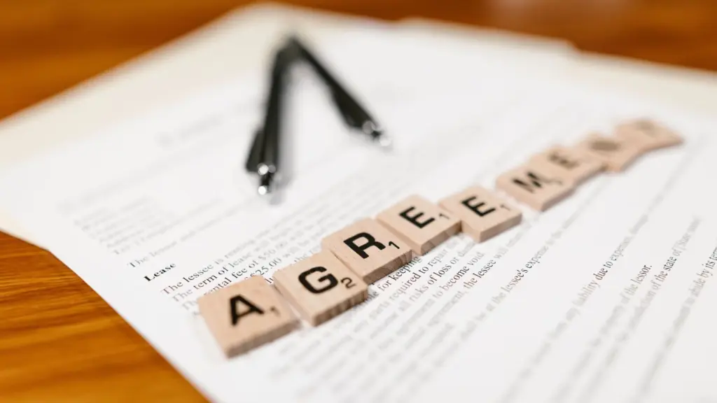 A lease agreement to symbolize a Memorandum of Understanding with scrabble ties spelling out the word agreement, two pens are laid over the agreement on a wooden table.