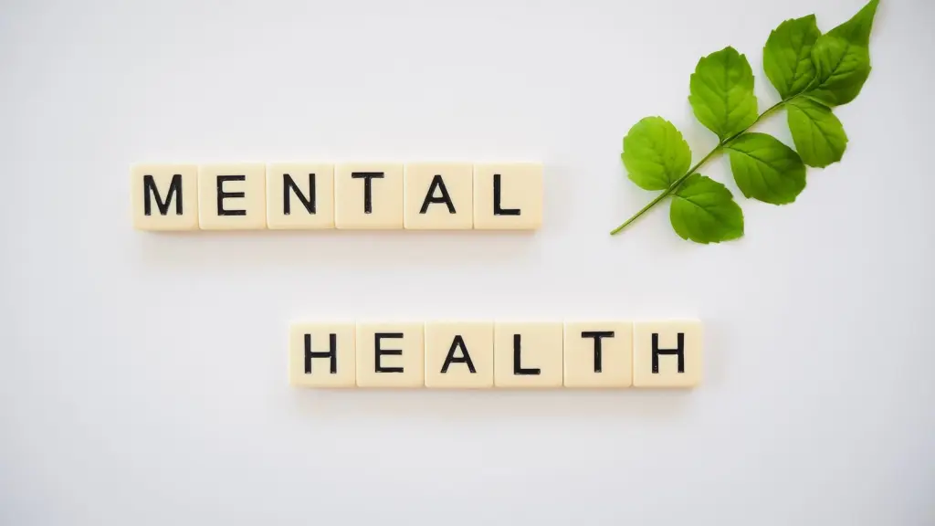 Scrabble tiles that read "Mental Health" on a white background with a green branch with leaves