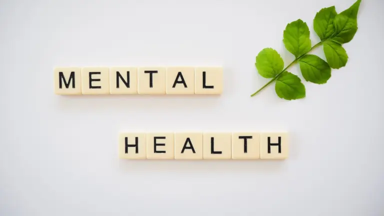 Scrabble tiles that read "Mental Health" on a white background with a green branch with leaves