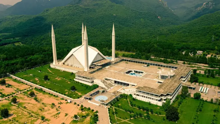 Aerial view of Shah Faisal Mosque in Islamabad, Pakistan in lush green surroundings, set against a backdrop of mountains.